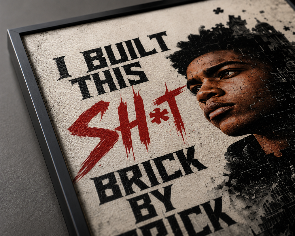 A framed poster print featuring a close-up portrait of a Black man on the right and bold text reading 'I BUILT THIS SH*T BRICK BY BRICK' on a distressed off-white background. The frame is dark gray, and the print is photographed against a neutral gray wall.