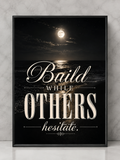 A framed motivational art print featuring a night ocean scene with a full moon and the quote 'Build WHILE OTHERS hesitate.' in cream lettering, shown leaning against a light gray marble wall.
